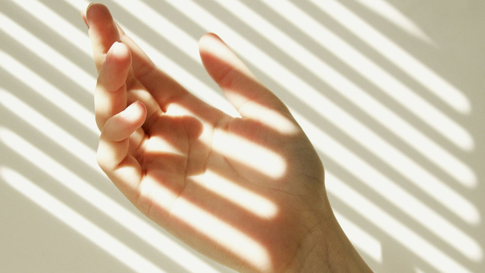 Morning sunlight through window blinds falling across an open hand, the daylight the skin uses to make vitamin D3